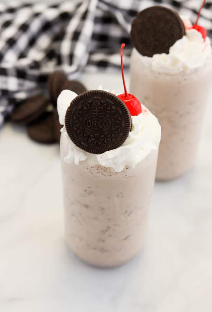 2 Oreo Milkshakes in glasses topped with Oreo cookie, whipped cream and a cherry.
