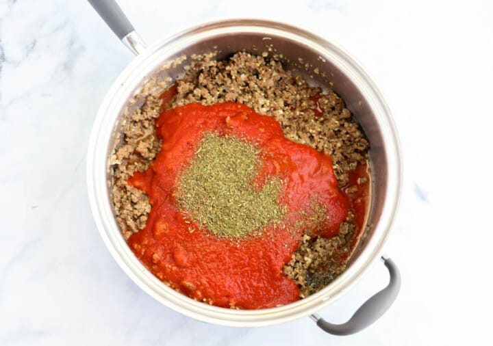 adding tomato sauce and seasoning to the ground beef.