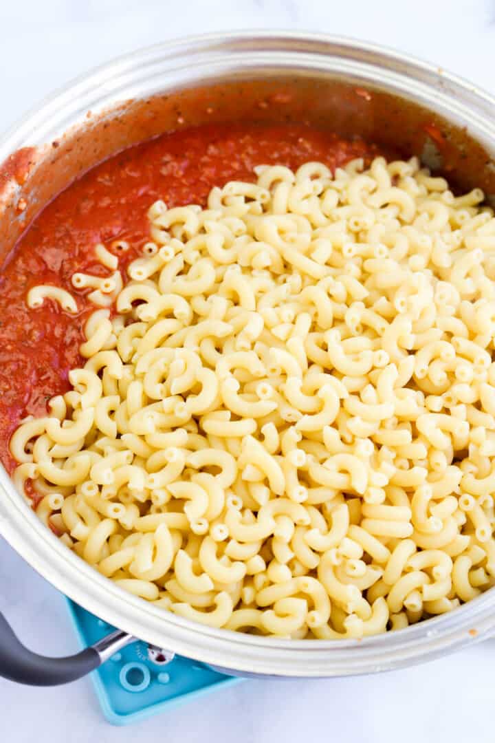 adding the cooked noodles to the large pot with sauce and beef.