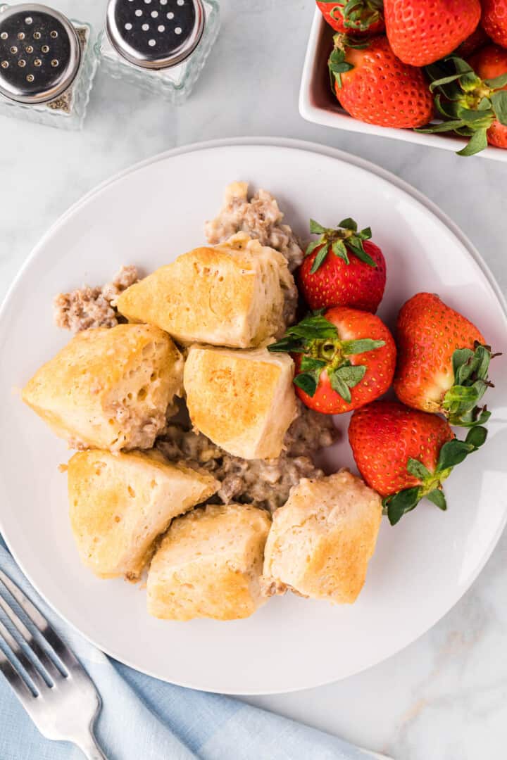 Biscuit and Gravy Casserole on white plate with strawberries.