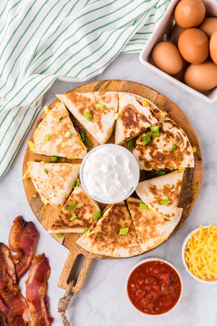breakfast quesadillas on wooden serving board with sour cream.