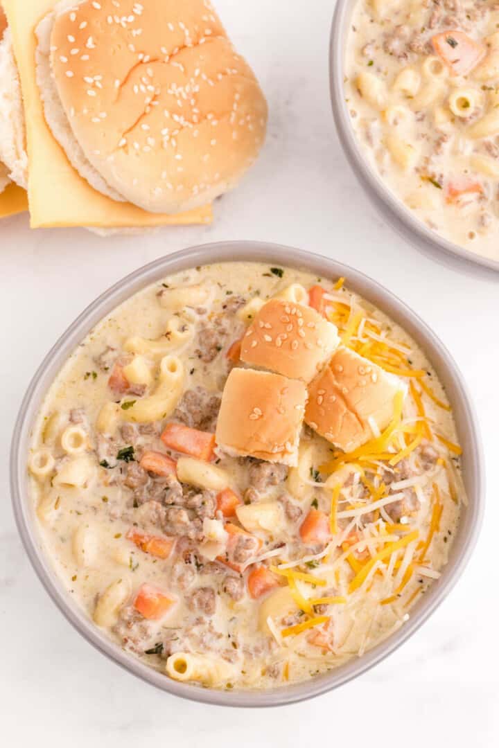 Cheeseburger Soup in bowl with hamburger bun on the side.