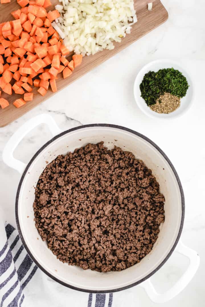 cooked ground beef with seasoning and veggies in the background.