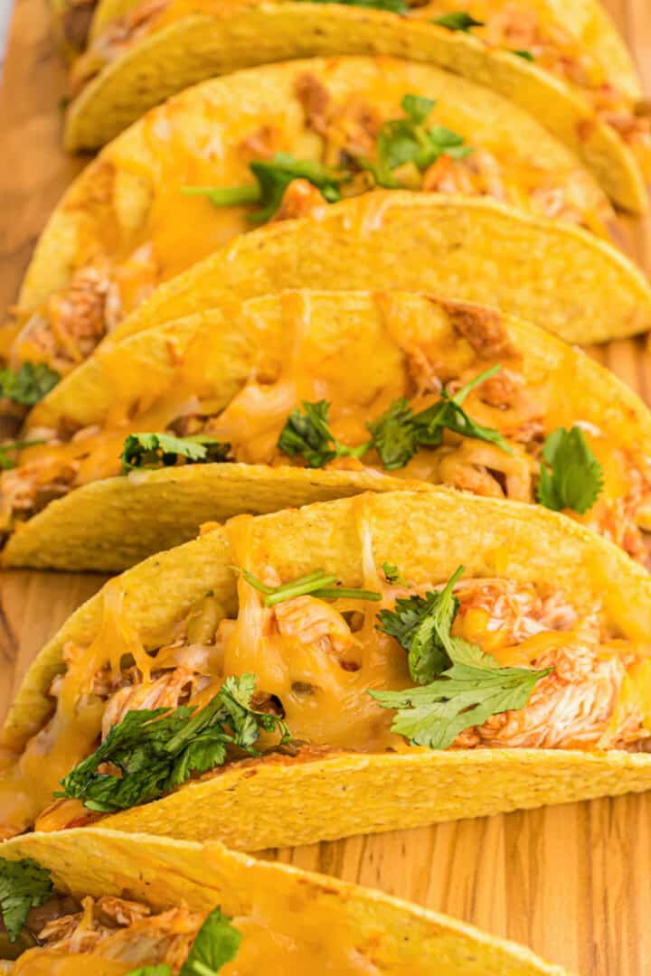 closeup of baked chicken tacos on wooden serving board.