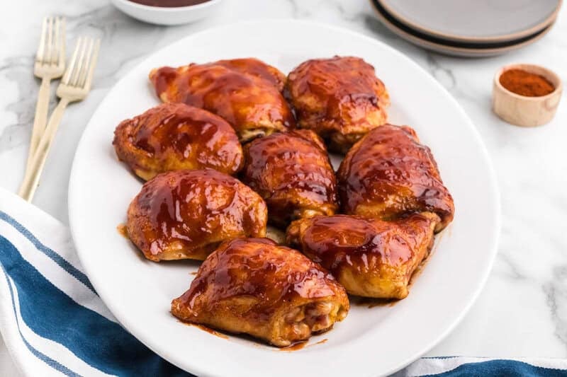 Baked BBQ Chicken Thighs on a white platter with navy hand towel next to it.