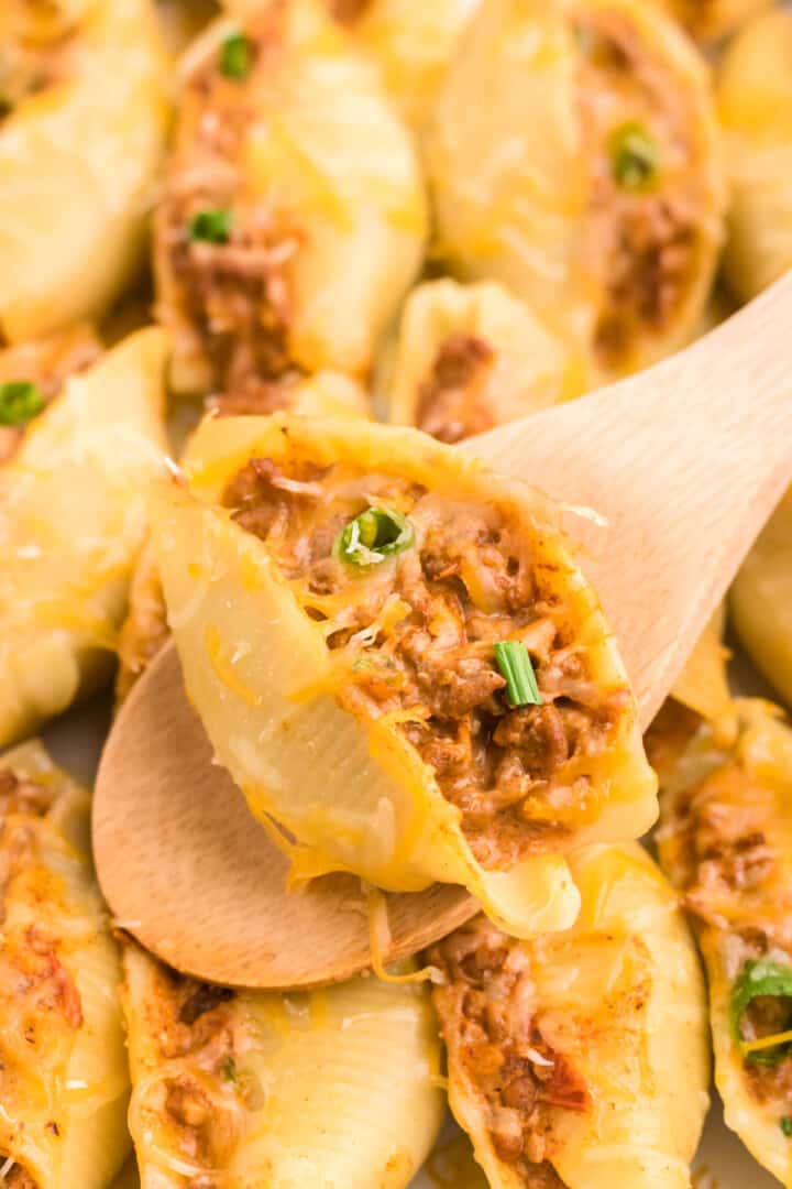 serving taco stuffed shells with wooden spoon.