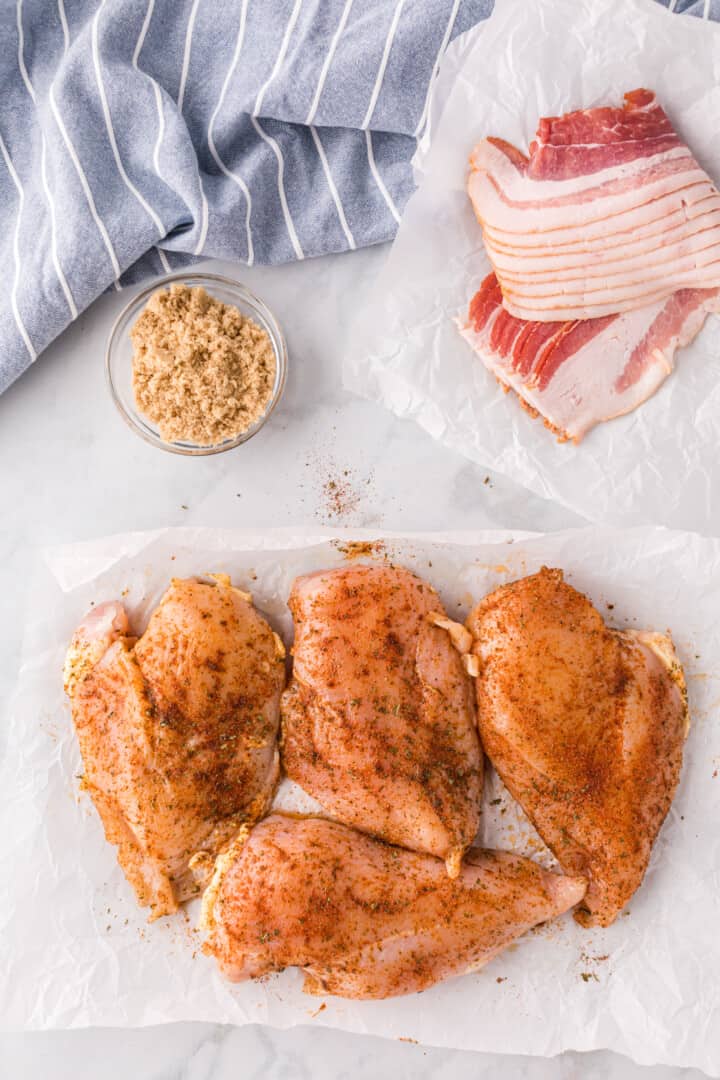 seasoned chicken breasts with bacon ready to wrap it.