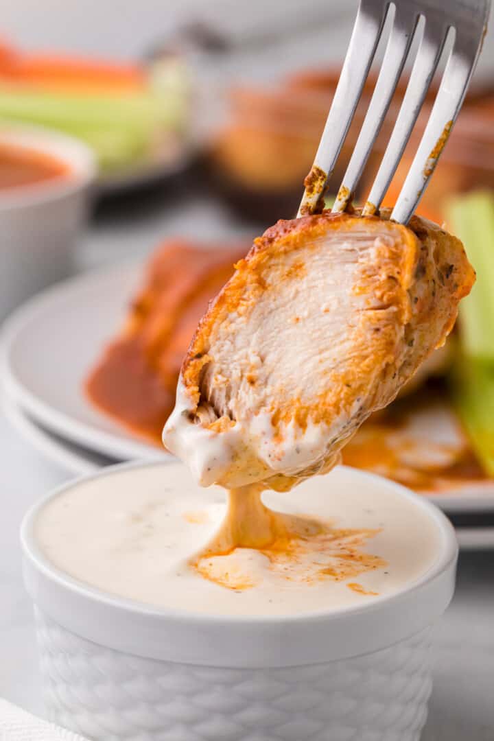 dipping piece of baked Buffalo chicken into ranch dressing.