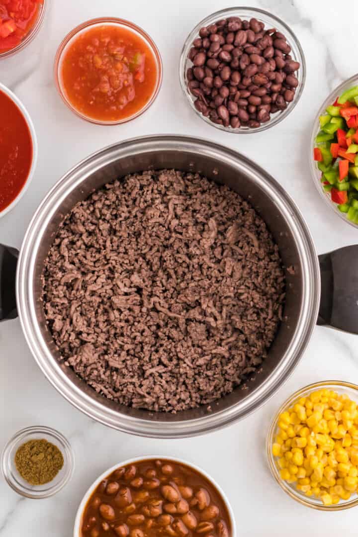 cooked ground beef in pan with other ingredients in bowls around it.