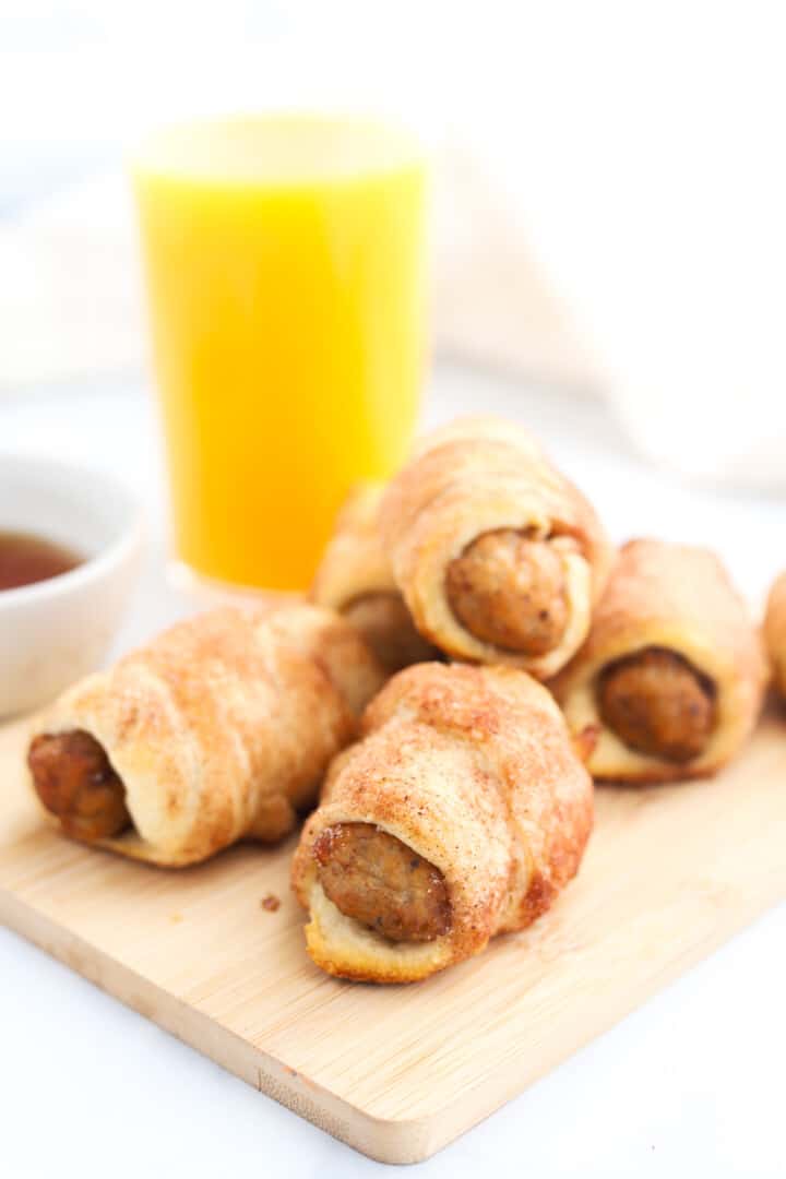 breakfast pigs in a blanket on wooden serving board with orange juice.