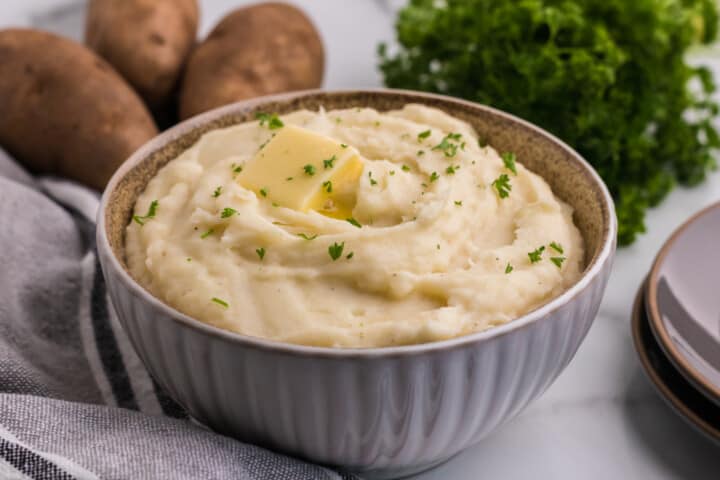 closeup of mashed potatoes in bowl with butter on top.