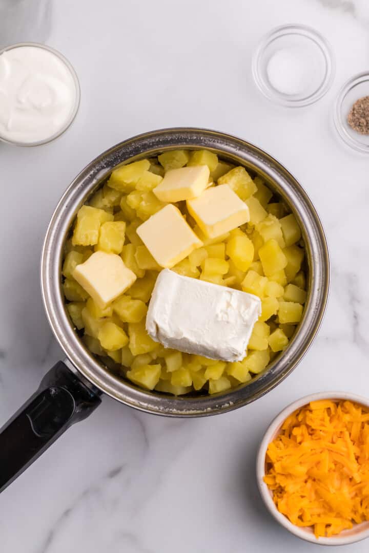 adding butter and cream cheese to the potatoes.