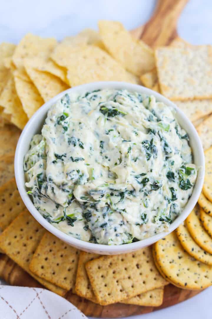 cheesy spinach dip in serving bowl with crackers around it.