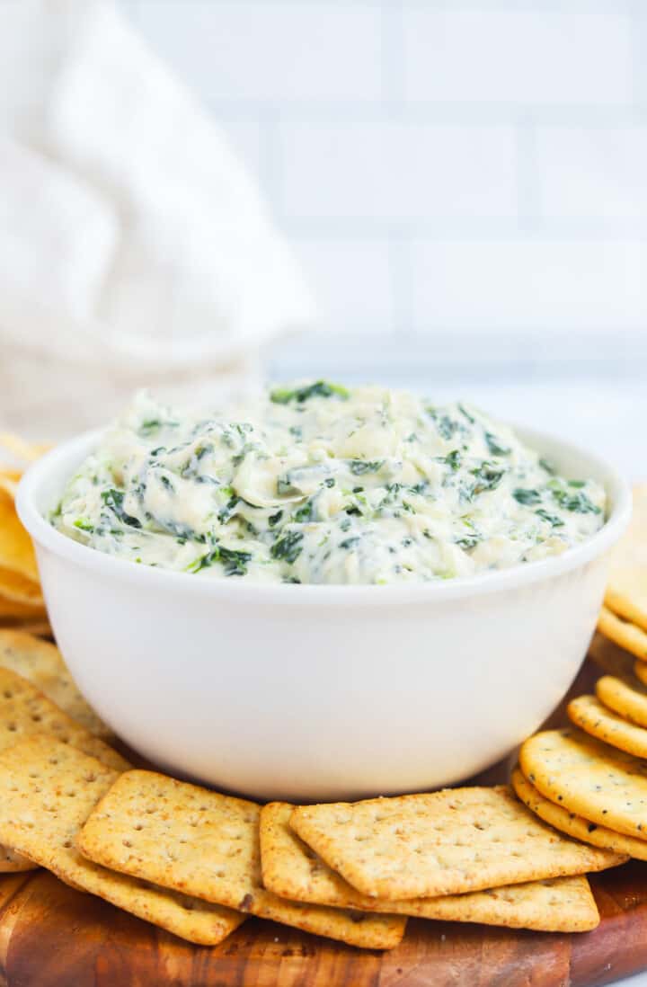 Cheesy Spinach Dip in white bowl with crackers around it.