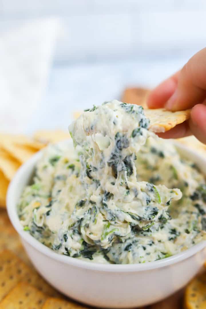 using a cracker to eat the spinach dip.