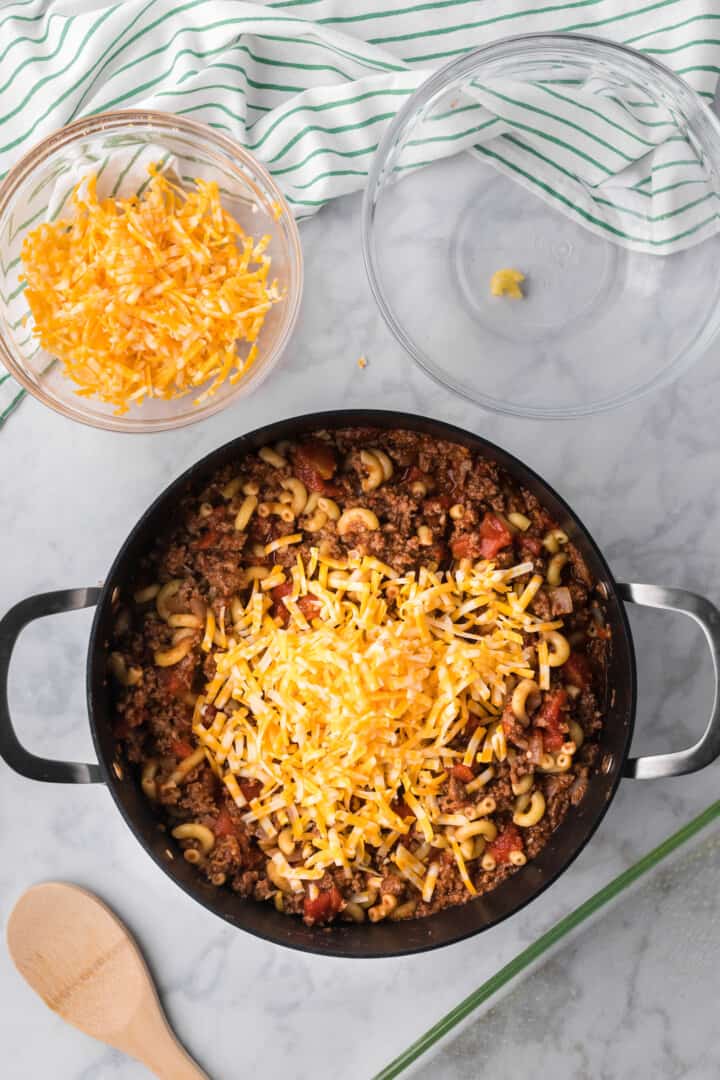 adding cheese and noodles to the ground beef pot.