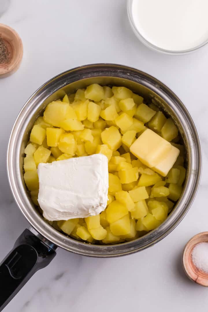 adding cream cheese and butter to the cooked mashed potatoes.