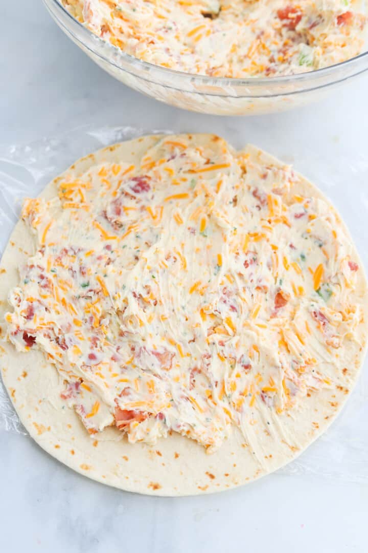 spreading the bacon ranch cream cheese mixture on to tortillas.