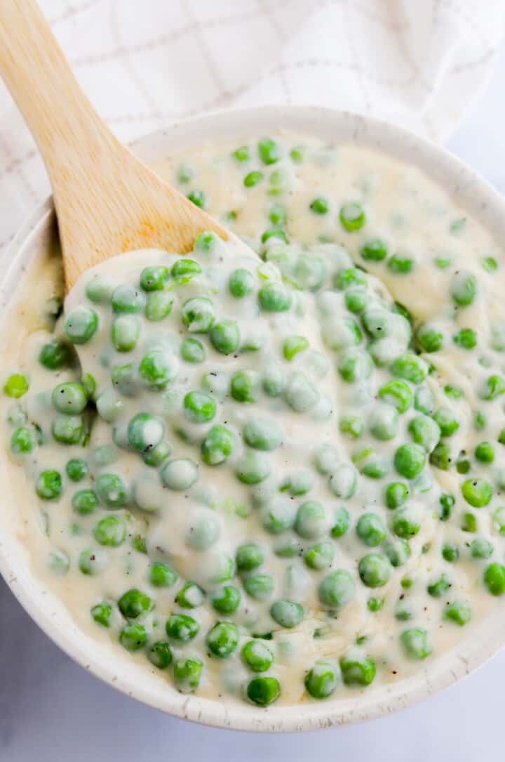 Creamed Peas in white serving bowl with wooden spoon.