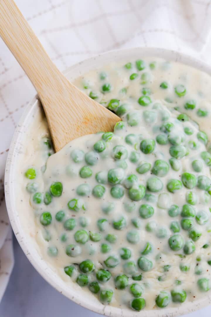 closeup of creamed peas in white bowl with wooden spoon.