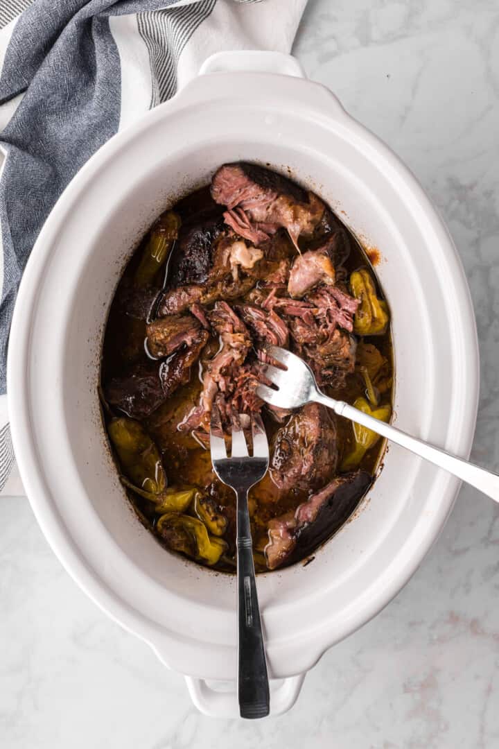 shredding the roast in the slow cooker.