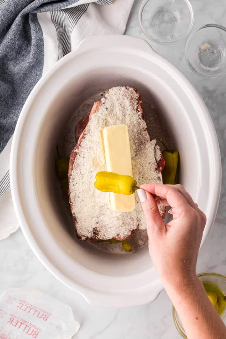 adding the butter and pepperoncini to the slow cooker.