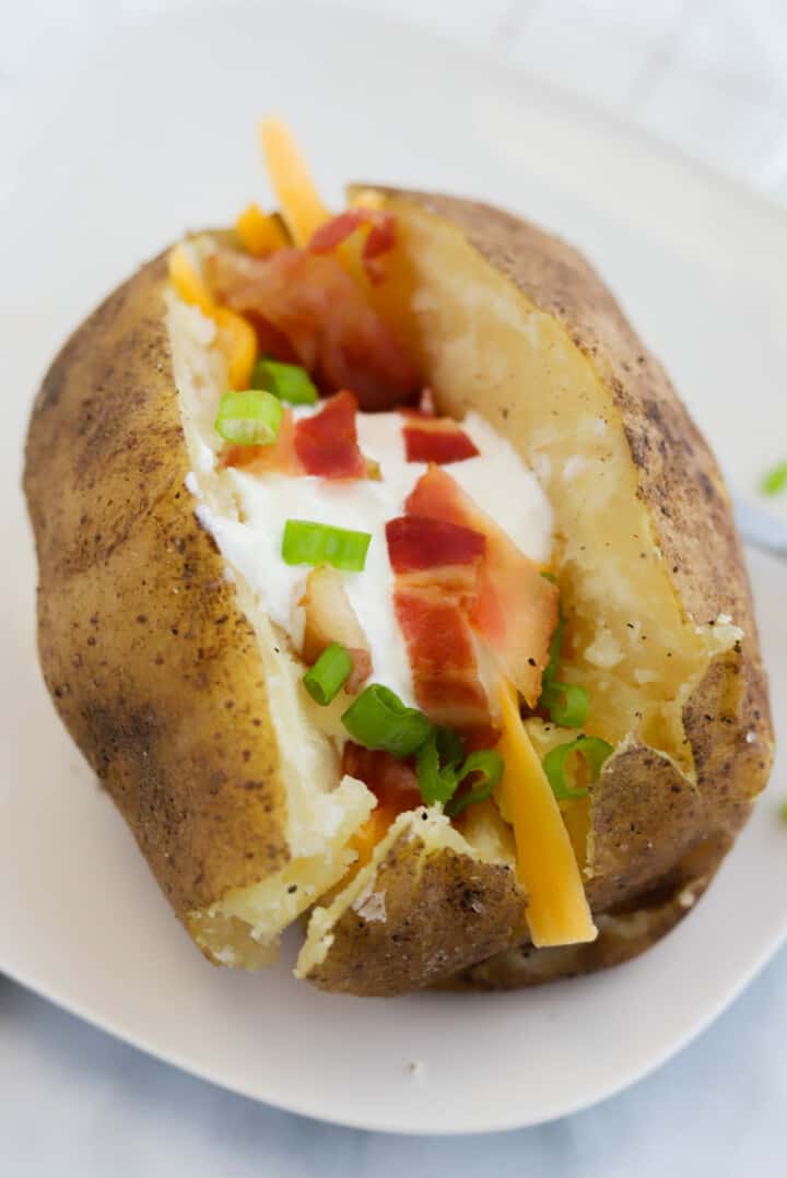 Slow Cooker Baked Potato on white plate topped with sour cream, bacon, cheese, and chives.