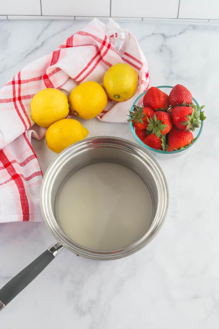 simple syrup in a pan with lemons and strawberries around.