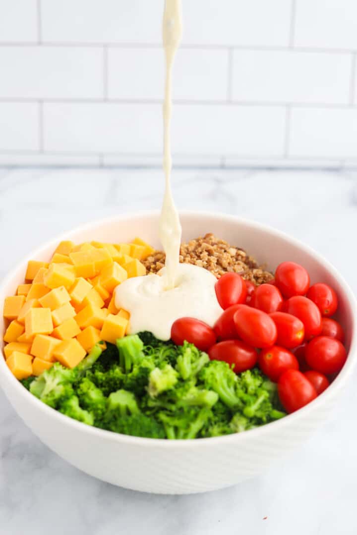 pouring the ranch dressing over the ingredients for the pasta salad.