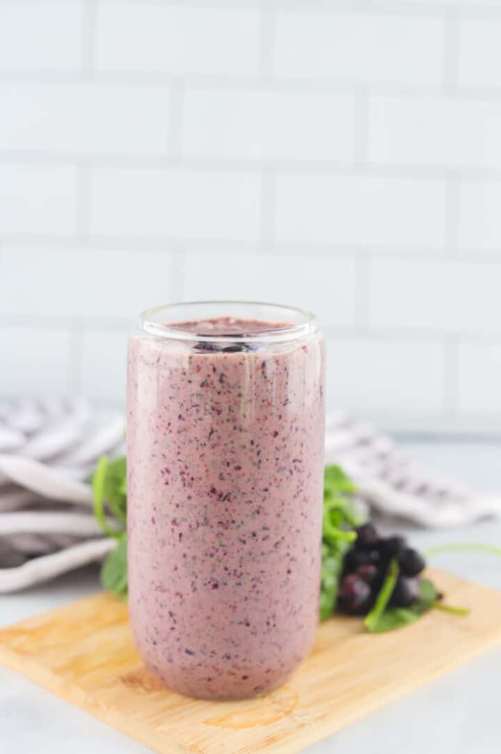 Blueberry Spinach Smoothie in glass on wooden serving board.