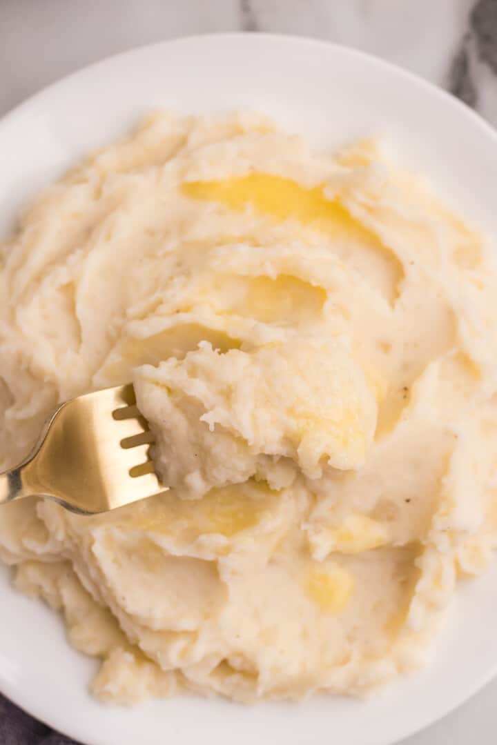 close up of mashed potatoes on white plate with fork.