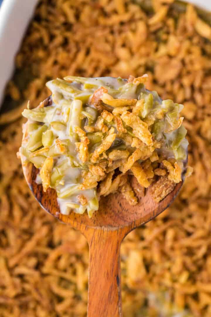 closeup of green bean casserole being served with a wooden spoon.