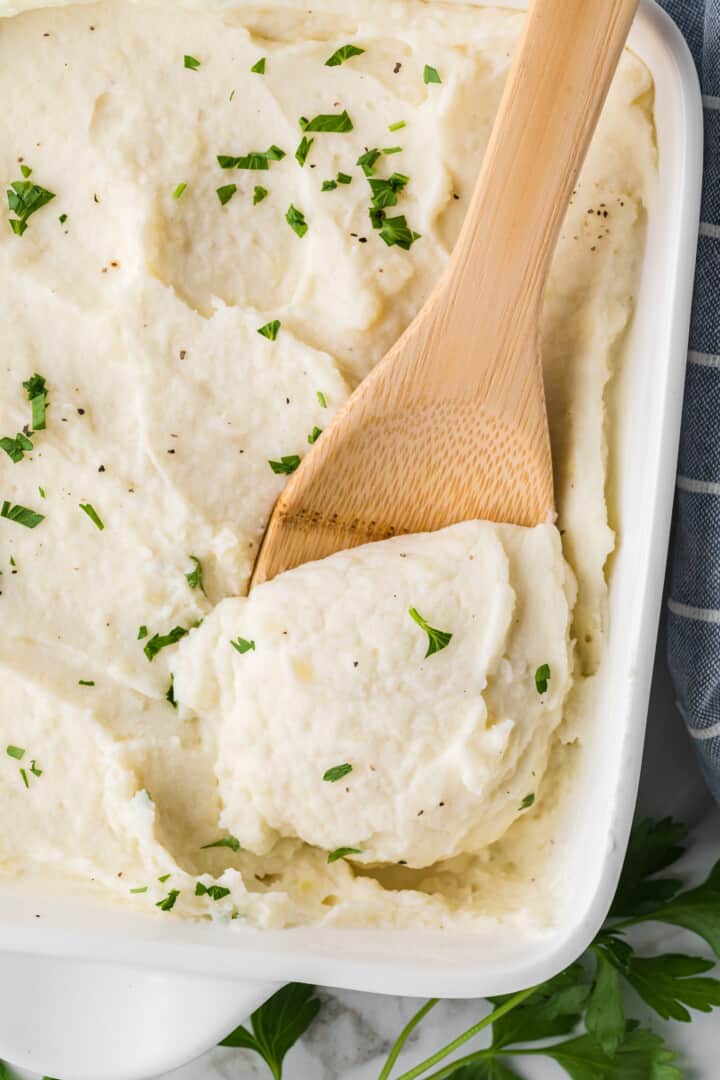 closeup of mashed potatoes being served with wooden spoon.