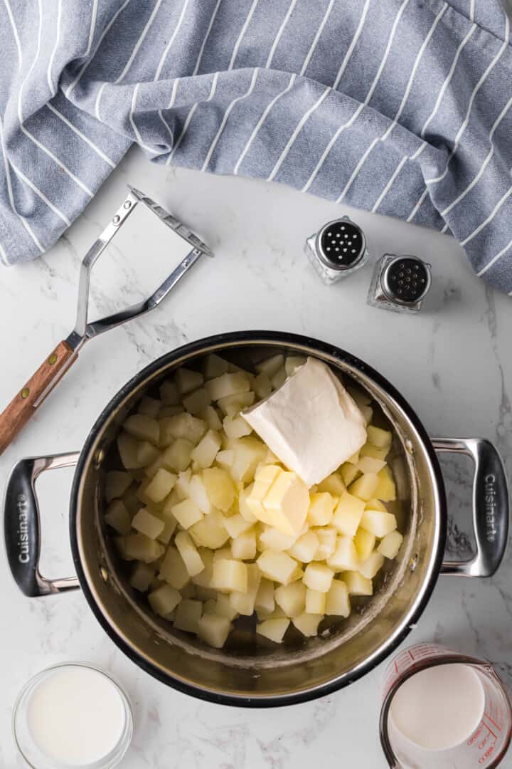 adding the cream cheese and butter to the cooked potatoes.