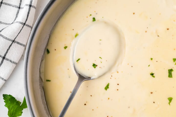 closeup of Alfredo sauce in a bowl with a spoon in it.