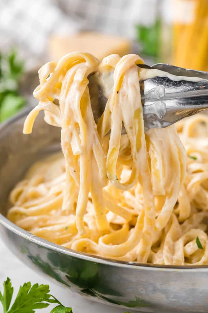 using tongs to serve the fettuccini alfredo.