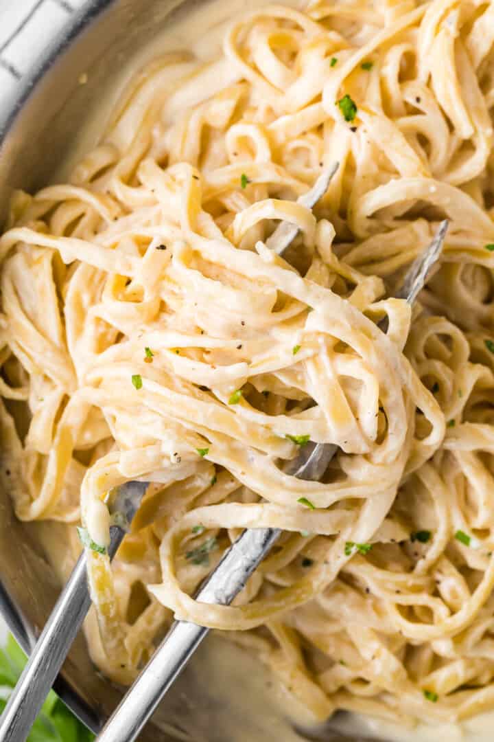 Pasta with homemade alfredo sauce being served with tongs.