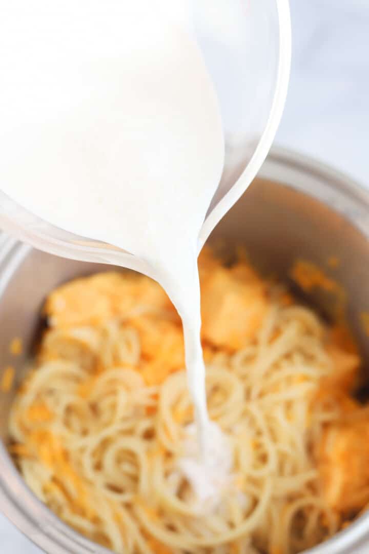 adding half and half to the cheesy spaghetti.