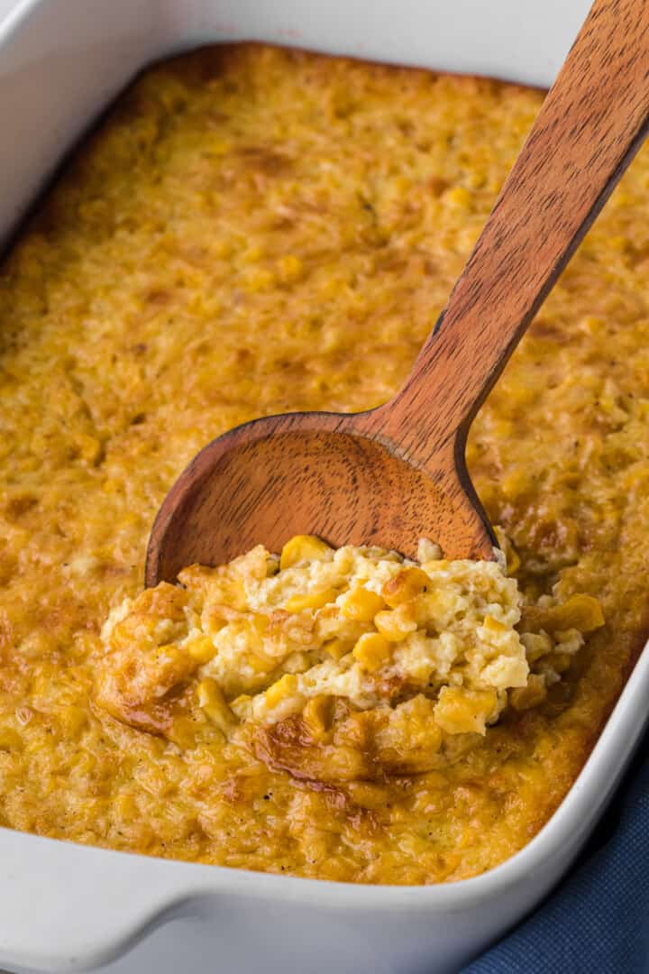 Corn Pudding in white casserole dish with wooden spoon.