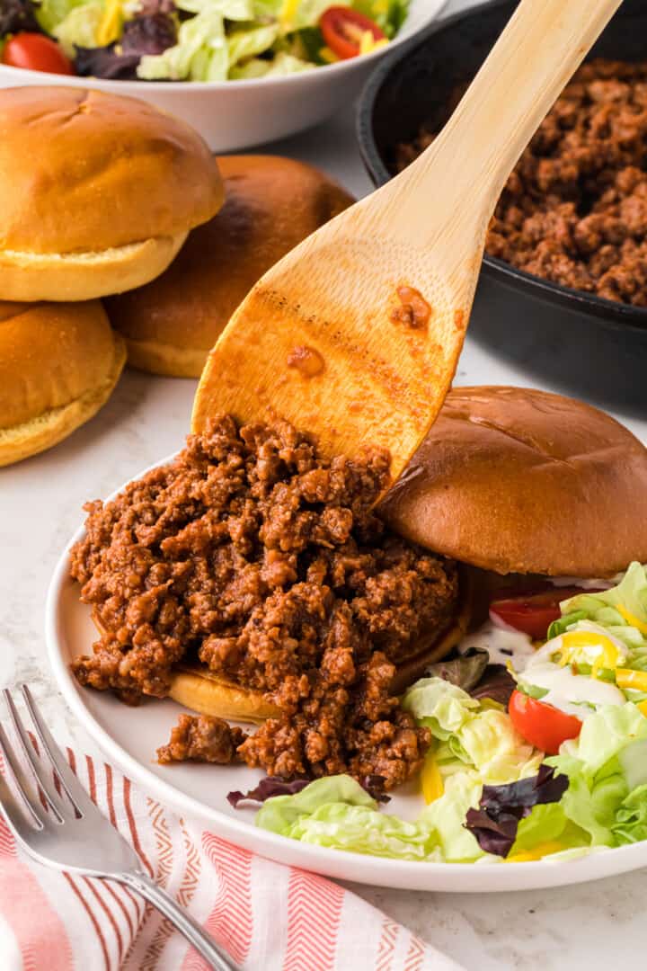 making a Sloppy Joe sandwich on a white plate.