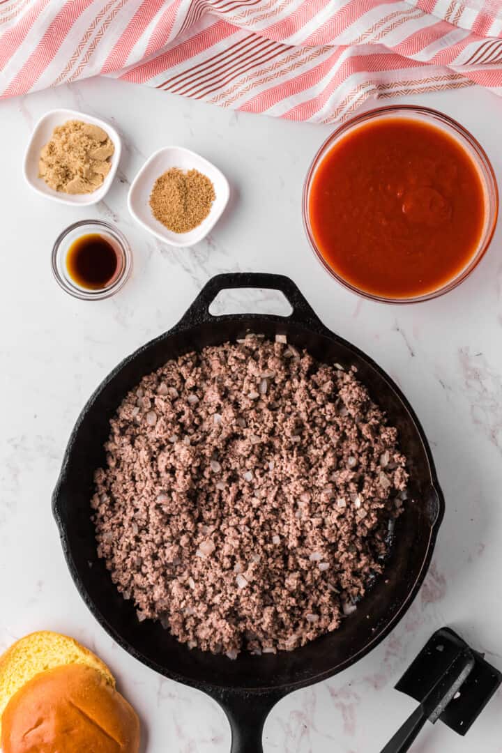 meat being cooked in skillet with other ingredients in bowls around skillet.