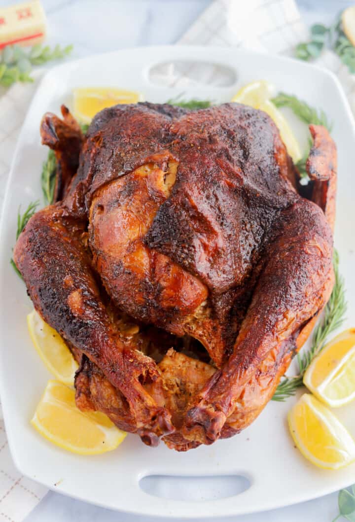 Smoked Turkey on white serving tray with garnishments around it.