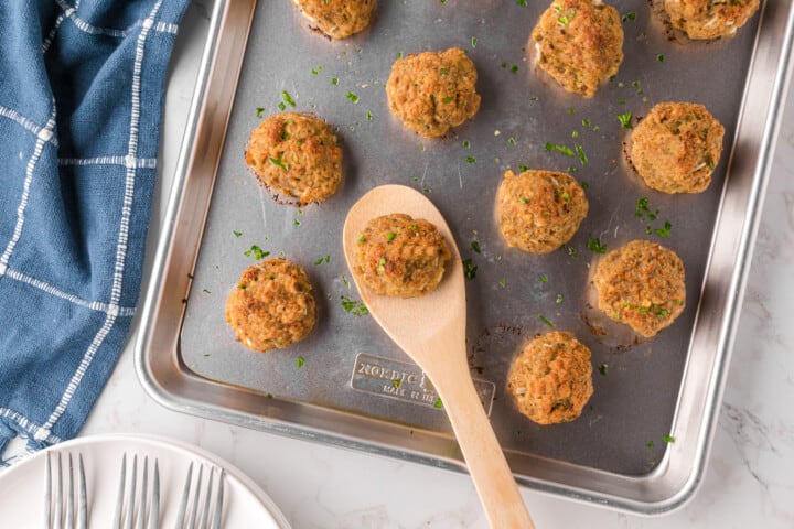 turkey meatballs on baking sheet being served with wooden spoon.