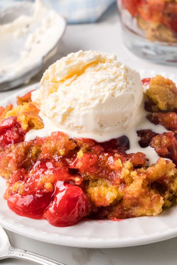 Cherry Dump Cake on white plate topped with ice cream.