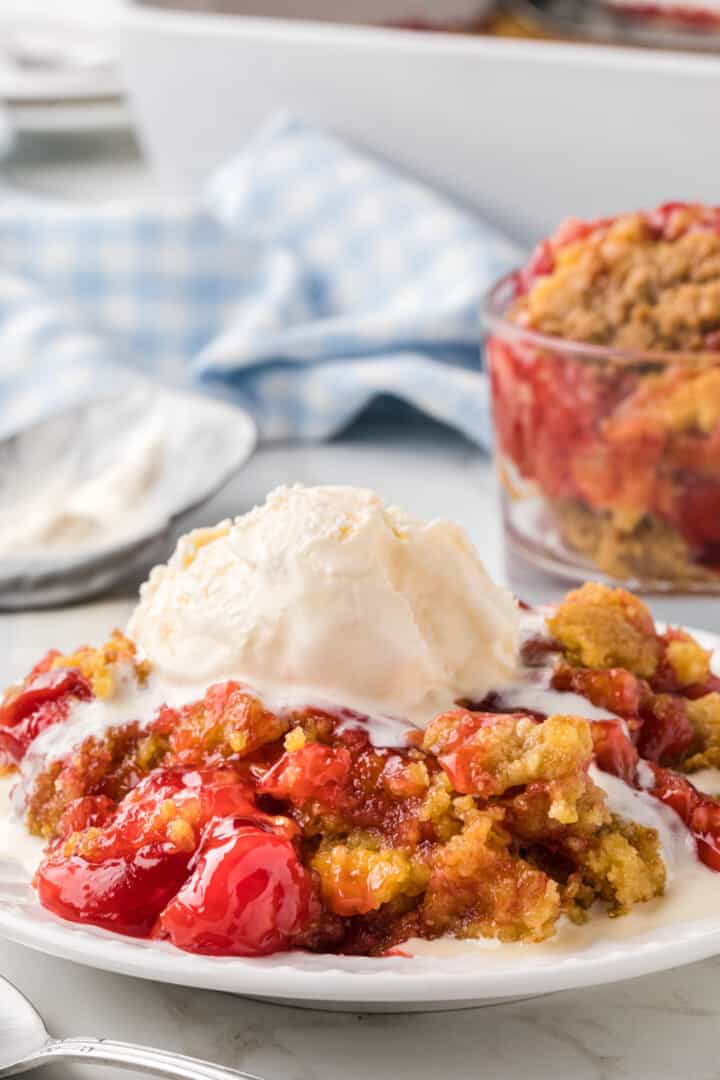 Cherry Dump Cake on white plate topped with ice cream.