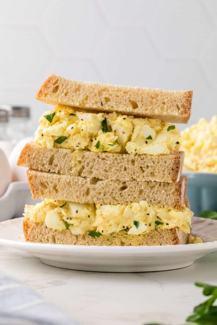 egg salad sandwich stacked on white plate.