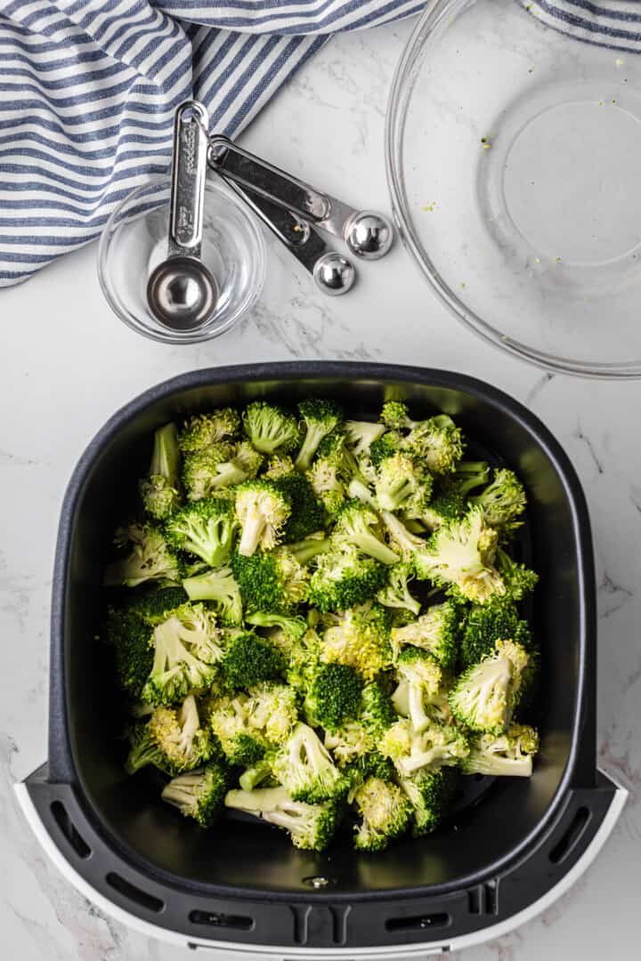 adding the broccoli to the air fryer basket.