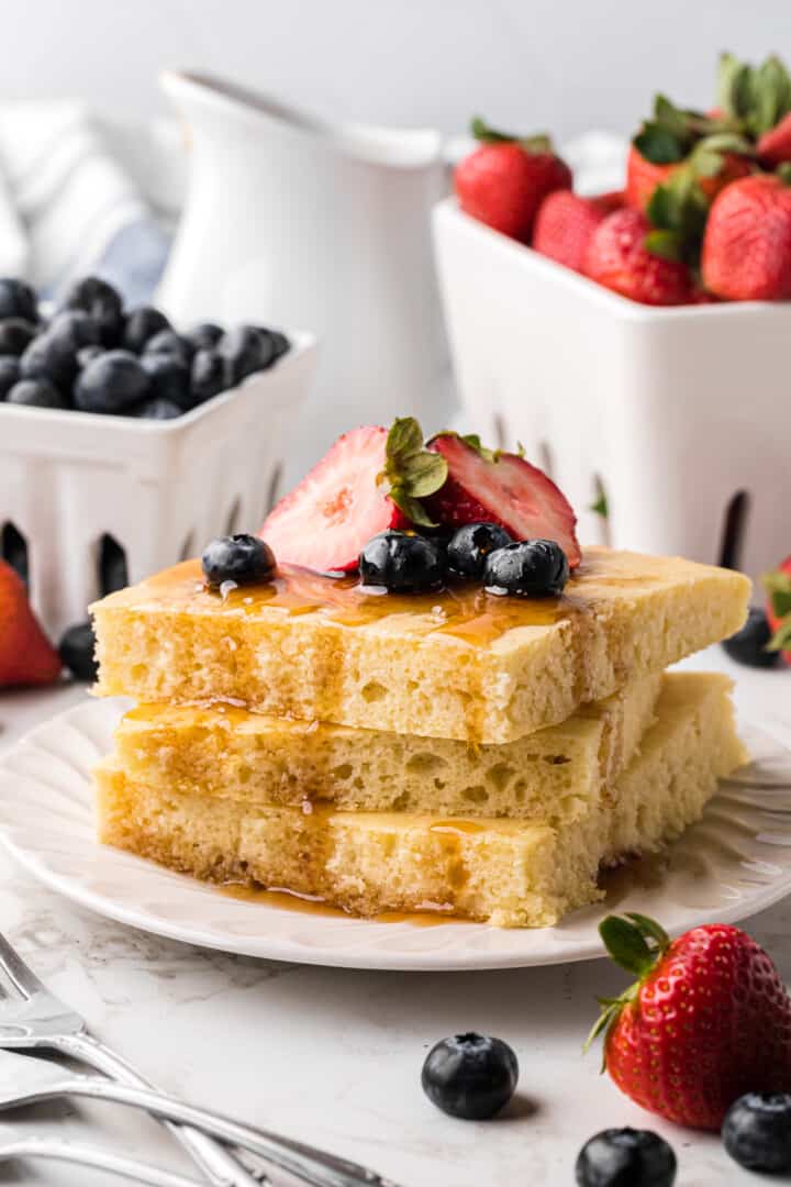 Sheet Pan Pancakes stacked on white plate topped with fruit.