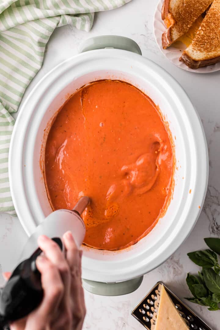 using an immersion blender to blend the tomato soup.