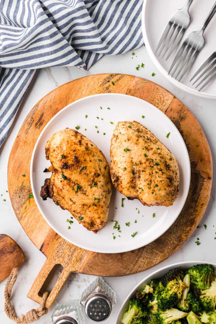 two chicken breasts cooked in the air fryer on white dinner plate.